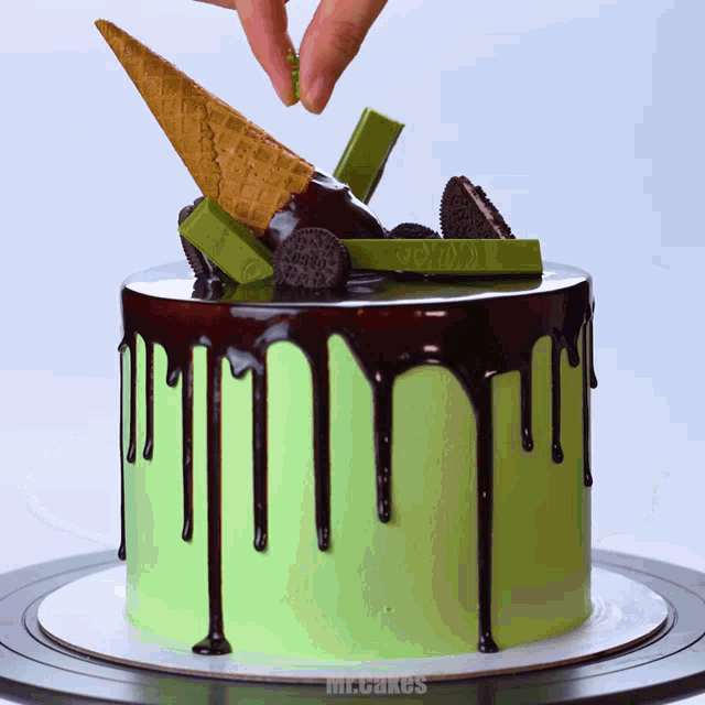 a green cake with chocolate drips and a kitkat cone on top