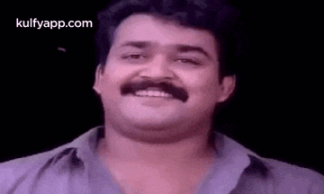 a man with a mustache is smiling in a purple shirt .