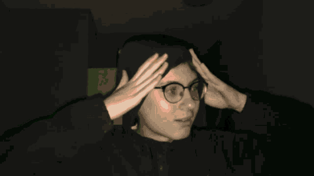a woman wearing glasses holds her hands to her forehead