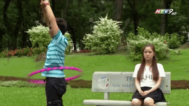 a woman sits on a bench while a man hula hoops in front of her
