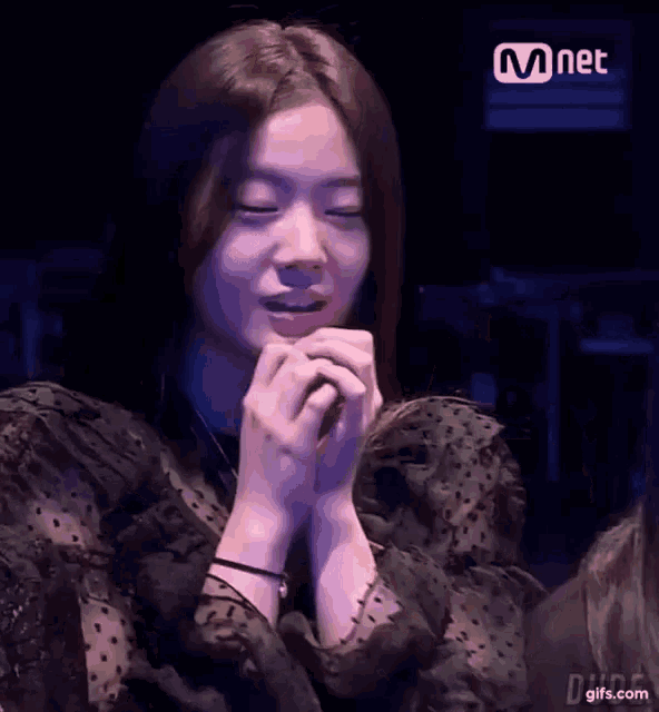 a woman in a black dress is sitting in a dark room with her hands folded in front of her face .