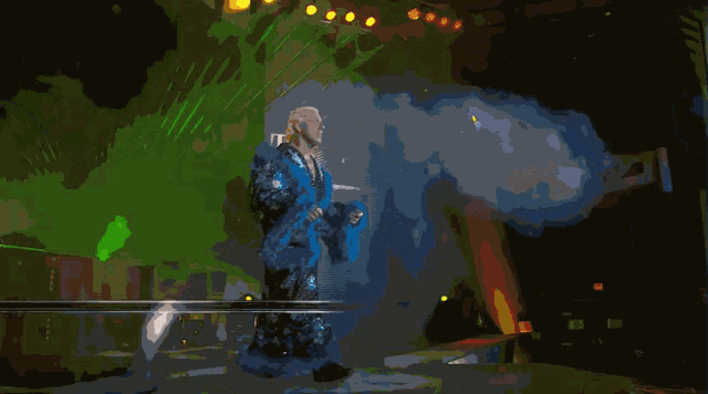 a man in a blue robe stands on a stage in front of a sign that says t.h.