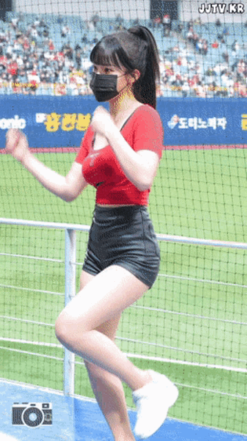 a woman wearing a mask is dancing on a baseball field in front of a banner that says jutv.kr