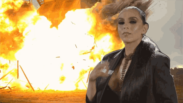a woman stands in front of a large explosion with a sign in the background that says ' i 'm sorry '