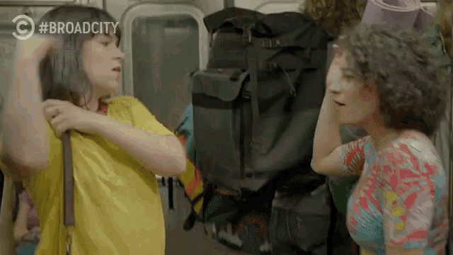 a woman in a yellow shirt is standing next to another woman in a pink hat with the word broadcity on the bottom