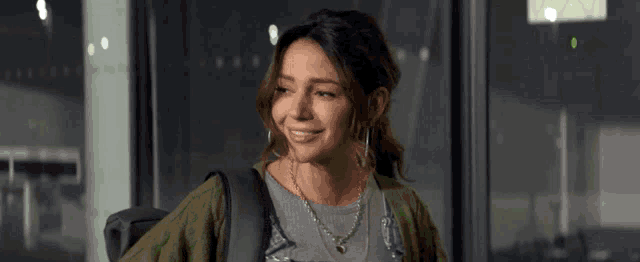 a woman wearing a gray shirt and a green cardigan smiles