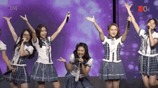 a group of girls singing into microphones in front of a screen that says live