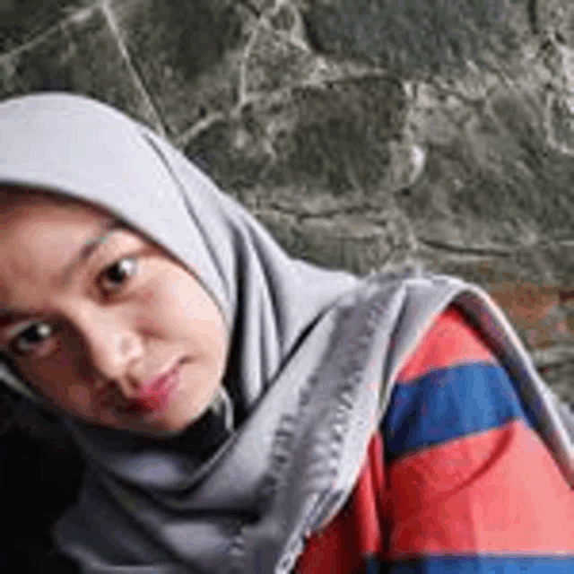 a young woman wearing a hijab and a striped shirt is looking at the camera .