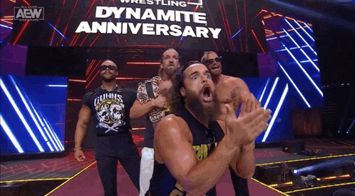 a group of men are standing in front of a sign that says dynamite anniversary .