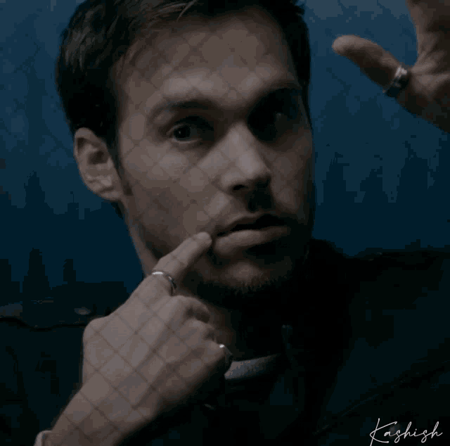 a man with a ring on his finger is behind a fence with kashish written on the bottom right