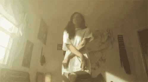a woman in a white dress is standing on a bed in a bedroom .