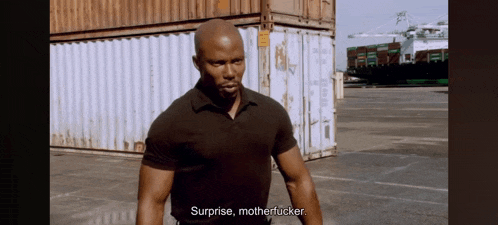 a man in a black shirt says surprise motherfucker in front of some shipping containers