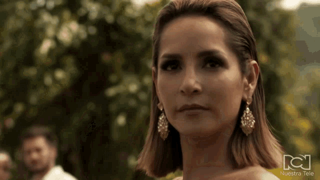 a woman wearing earrings is standing in front of a nuestra tele logo