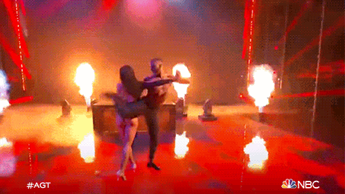 a man and a woman are dancing on a stage with flames behind them and a nbc logo in the corner