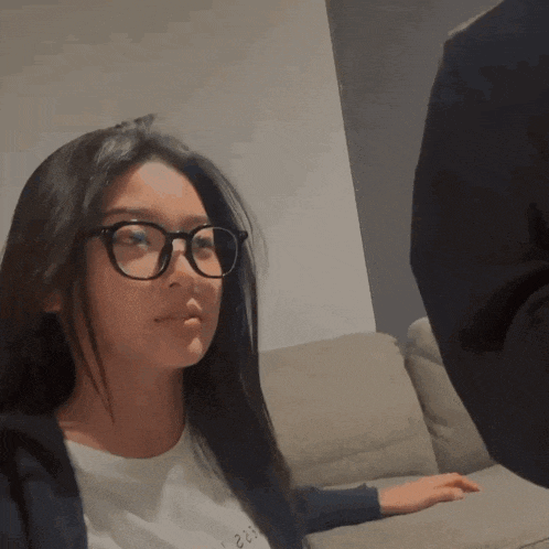 a woman wearing glasses is sitting on a couch with her hand on the arm of the couch
