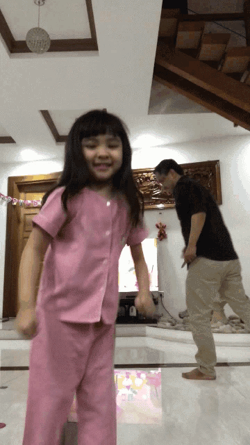 a little girl in pink pajamas is dancing with a man in khaki pants