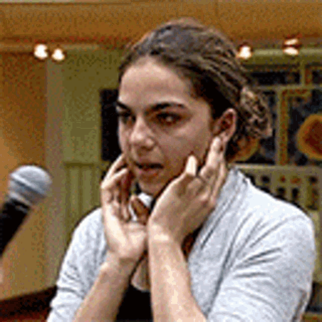 a woman is talking into a microphone while covering her face with her hands .