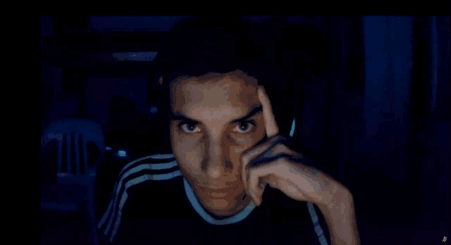 a man in a black shirt with white stripes on the sleeves holds his hand to his forehead