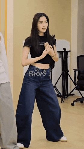 a woman in a black crop top and wide leg jeans has the word story written on her waist