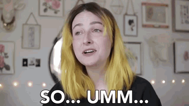 a woman with yellow hair is saying so umm in front of a wall of pictures .