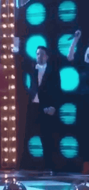 a man in a tuxedo is dancing in front of a wall of blue lights