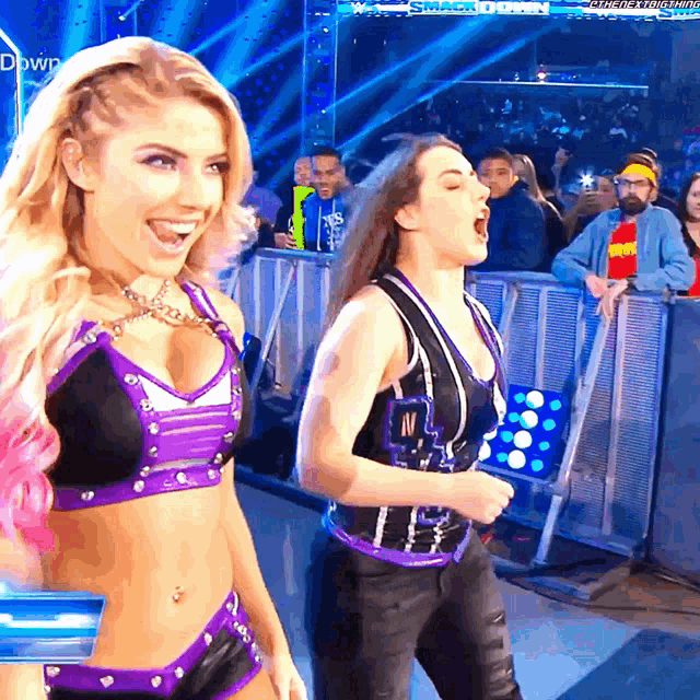 two women are standing in front of a crowd with a sign that says smackdown in the background