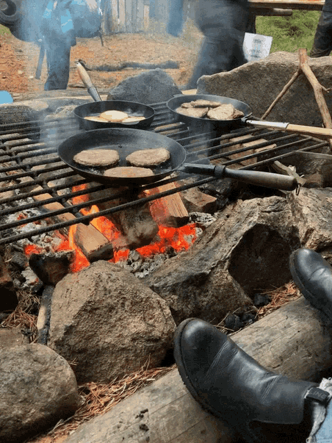 four pans of food are cooking over a fire
