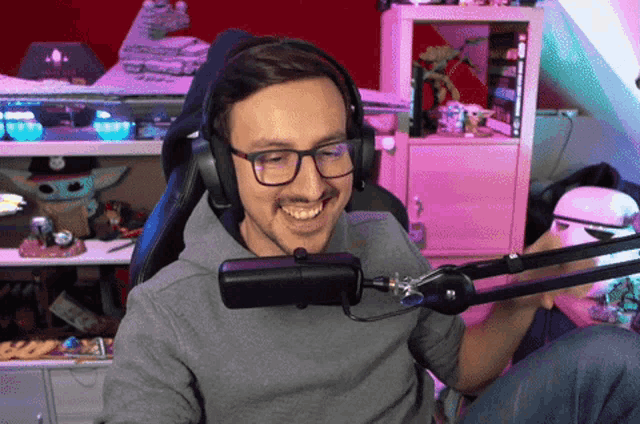 a man wearing headphones and glasses smiles while sitting in front of a microphone