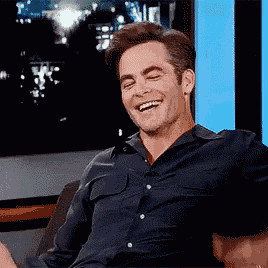 a man in a black shirt is sitting on a couch laughing .