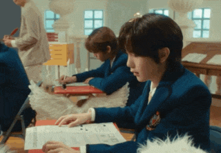 a boy in a school uniform is sitting at a desk with a piece of paper that says ' a ' on it