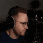 a man with a beard wearing headphones and glasses is sitting in front of a microphone .