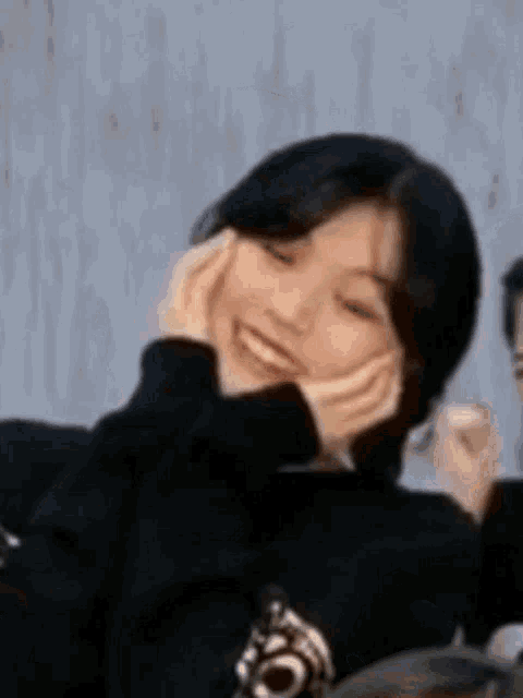 a woman is smiling with her hands on her face while wearing a black sweater .