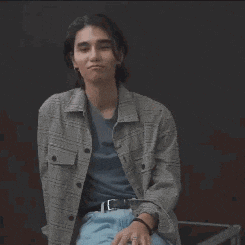 a young man in a plaid jacket and blue jeans is making a face .