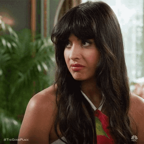 a woman with long hair and bangs is sitting in front of a plant and making a funny face .
