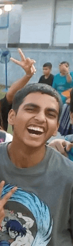 a young man is laughing and giving a peace sign while wearing a t-shirt .