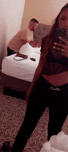 a woman is taking a picture of herself in a mirror with a man in the background