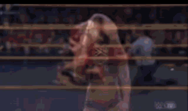 a blurry picture of a wrestling match in a ring with a crowd in the background .