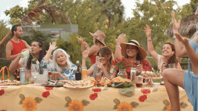 a group of people are sitting at a table with a floral table cloth