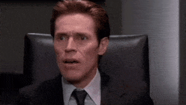 a man in a suit and tie is sitting in a chair making a funny face .