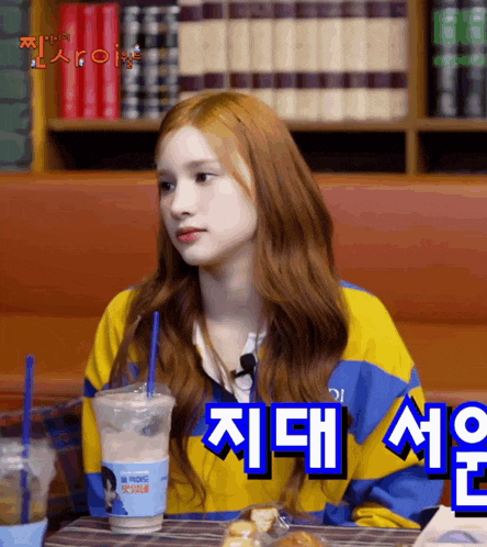 a girl with red hair is sitting at a table with a cup of coffee and a straw .