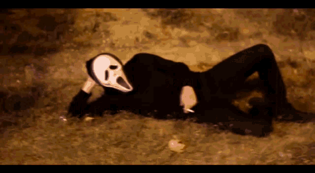 a person wearing a scream mask is laying in the grass smoking a cigarette .