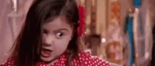a little girl with a red flower in her hair is making a face .