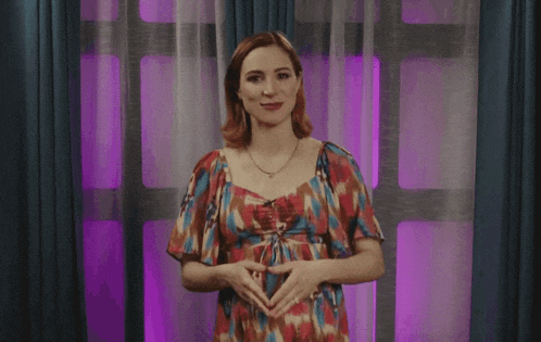 a woman in a floral dress is standing in front of a window with purple curtains