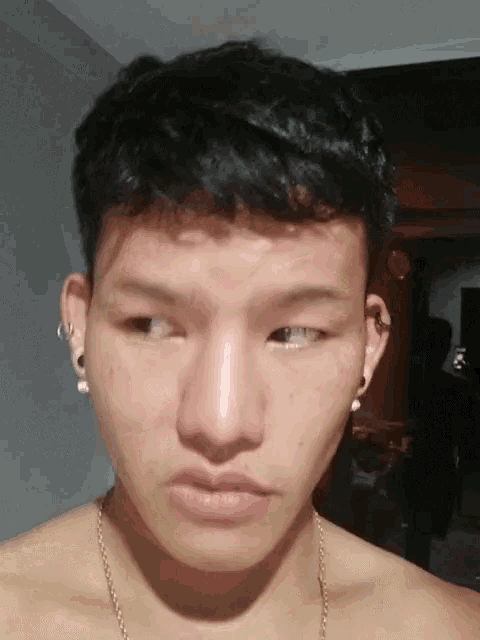 a young man without a shirt is wearing earrings and a gold chain around his neck