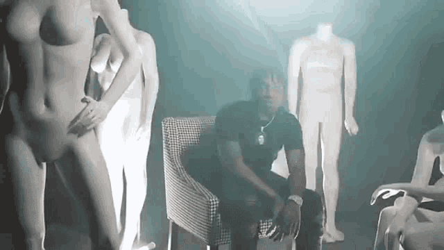 a man is sitting in a chair in front of a group of naked mannequins