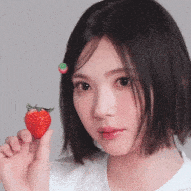 a woman is holding a strawberry in her hand and has a strawberry in her hair