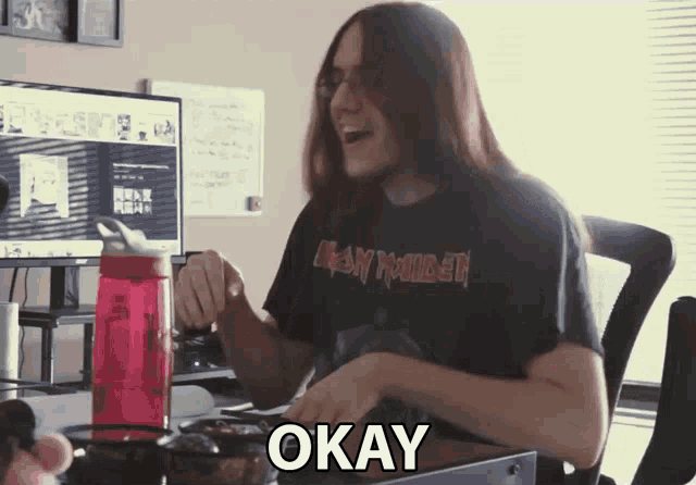 a man wearing an iron maiden shirt is sitting at a desk