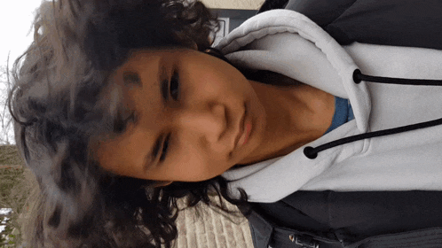 a young man with curly hair is wearing a grey jacket and a white hoodie