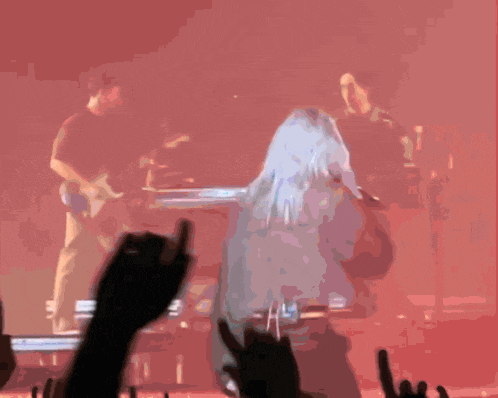 a woman with blue hair stands in front of a stage with a band