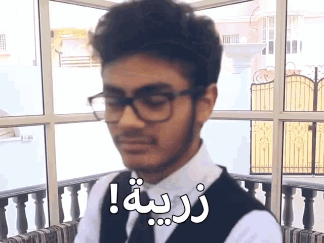 a man wearing glasses and a vest has arabic writing on his shirt